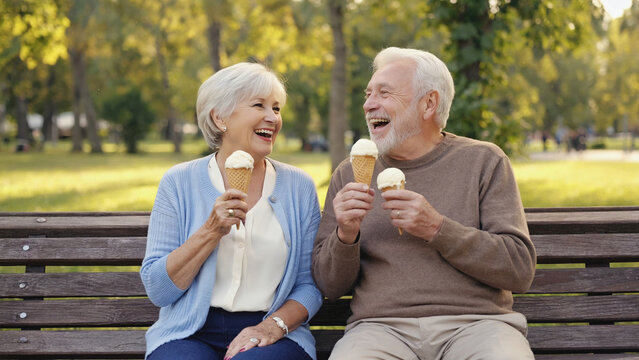 A couple shares a sweet moment eating ice cream cones while seated on a bench - Powered by Adobe