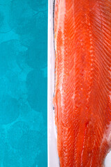 Whole salted trout fillet on white ceramic plate on blue background. Fresh seafood ingredient. Cooking red fish. Copy space