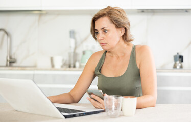 Woman chatting on internet using a laptop in domestic kitchen