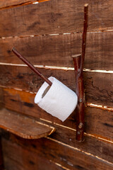 Toilet paper roll hanging on a handmade holder crafted from natural tree branches, fixed to a wooden wall in a rustic, eco-friendly bathroom setting