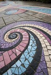 Colorful Mosaic Tile Pathway with Spiral Design Featuring Purple Pink Blue and Beige Tiles on a Concrete Surface in an Outdoor Setting