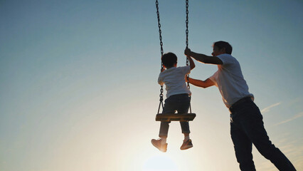 A father and child enjoy quality time on a swing during a beautiful sunset