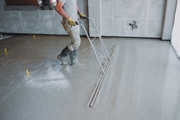 Construction worker leveling concrete surface flooring using bull float