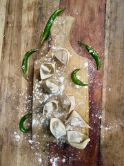 raw dimsum with flour powder and some green chilies on a wooden cutting board with a wooden table...