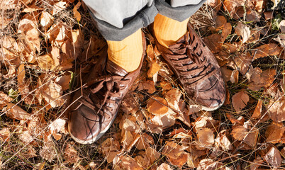 person in yellow socks and brown leather shoes walking on a forest floor scattered with dry autumn leaves, reflective outdoor moment, walking in forest, nature season
