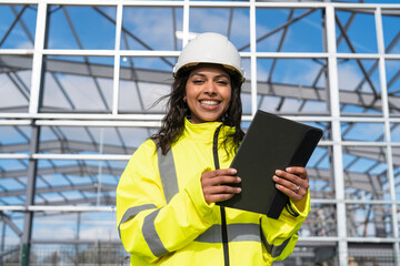 Portrait of happy smiling female construction worker builder with tablet, dressed in high...