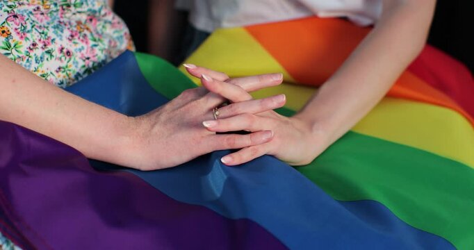 Close up lesbian couple in love holding hands on rainbow flag. Lgbt family holding hands outside. Woman relationship, lgbt family concept.