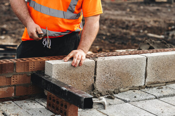 Skilled bricklayer working on construction site laying concrete footing blocks for wall construction