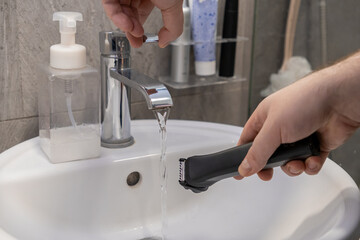 Male hand cleaning an electric shaver under fresh running water from a chrome faucet in a white...