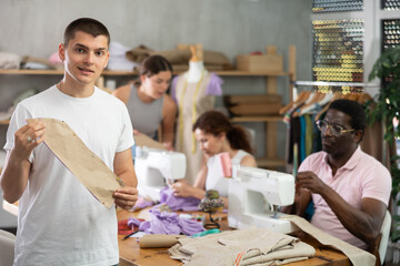 Positive young guy holding textile detail fixed on paper in dressmaking courses