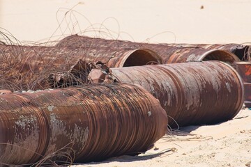 Rusty abandoned industrial pipes and wires polluting a sandy beach, highlighting environmental...