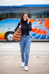 cheerful travel woman walking while talking on phone with a bus in the background