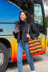 smiling woman walks beside a colorful bus while holding mobile phone