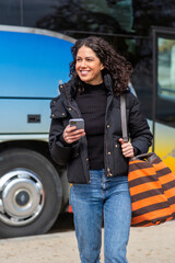 woman walking near colorful bus, smiling while holding her phone