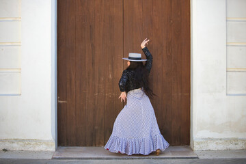 Latin woman, young and beautiful dancing flamenco in front of a wooden door in a typical street of...