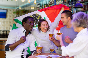 Cheerful diverse soccer supporters holding the flag of Mexico and enjoing beer in the sport bar