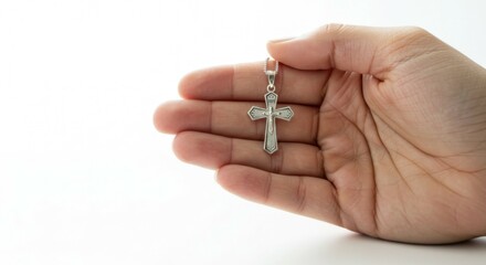 Hand presenting small cross necklace against neutral backdrop. Copy space