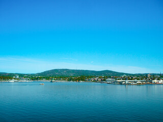 Oslofjord in Oslo, Norway, stretches beneath a clear sky with calm blue waters, green hills, and a vibrant cityscape—blending natural beauty with urban elegance.