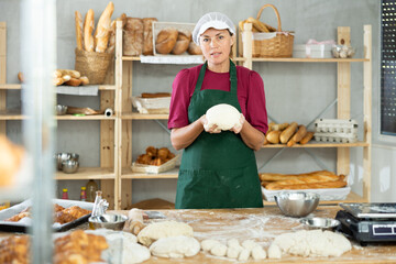 Woman works in bakery as baker, kneads dough, works with flour. Working moment, process of creating...