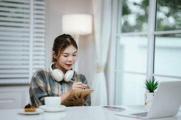 A young woman wearing headphones reads a book peacefully at home, enjoying a quiet study moment in...