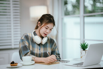 A young woman wearing headphones reads a book peacefully at home, enjoying a quiet study moment in...