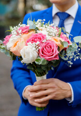 Groom in a blue suit holding a wedding bouquet. Close-up of hands and floral arrangement, no face visible. Elegant composition with focus on romantic detail and emotional symbolism.