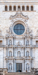 Close-up of Girona Cathedral’s ornate Baroque facade with intricate stone carvings, statues, and a rose window, Spain. Features sacred sculptures, decorative details, and 1733 date inscription