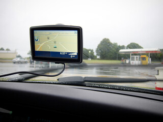 A generic Satnav system mounted on the window of a car, on a wet day near a gas station