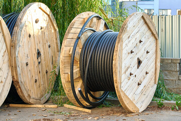 Coiled wire stored on large round wooden spools prepared for electric or telecom network deployment...