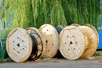 Large wooden cable reels stacked at construction site prepared for power installation, bundled spools of industrial wire under daylight. Multiple wooden drums stored at an outdoor construction zone