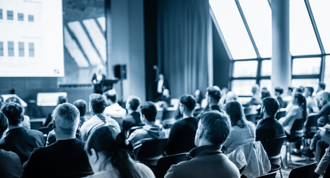 Speaker giving a talk in conference hall at business event. Blue toned black and white image