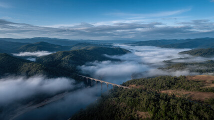 Obraz premium breathtaking aerial view of mountains shrouded in morning fog with delicate bridge spanning deep valley