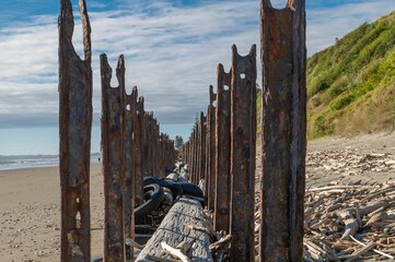 Rusty metal beams on a sandy beach with driftwood.