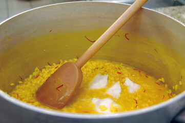 Chef adding butter to saffron risotto in large pot with wooden spoon