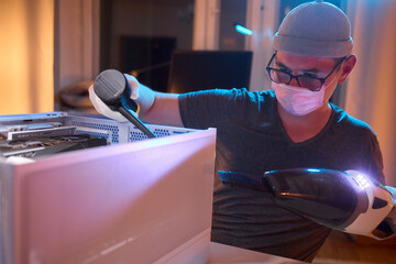 A man cleans a computer case with a vacuum in a bright room, stressing workspace tidiness