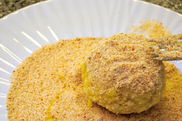 Chef breading a potato croquette with breadcrumbs on white plate