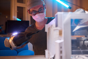A man cleans a computer case with a vacuum in a bright room, stressing workspace tidiness