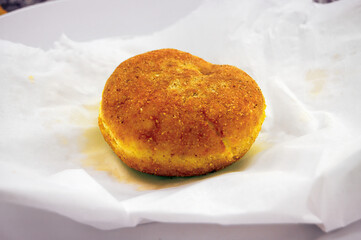 Freshly baked fritter resting on white paper on a white plate