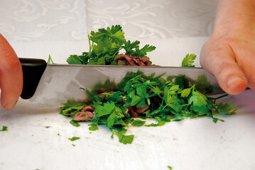 Chef chopping anchovies and parsley with knife on cutting board