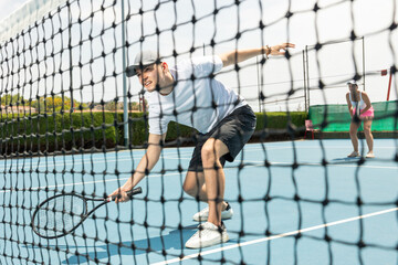 Portrait of man playing with male partner tennis doubles game on outdoors court. View through the tennis net