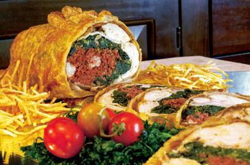 Sliced puff pastry stuffed chicken with spinach and speck, garnished with potato straws and tomatoes