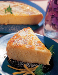 Slice of rice pudding cake with icing sugar and lemon zest on blue plate