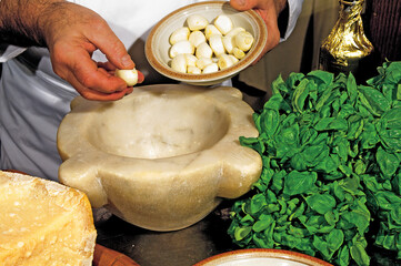 Chef adding garlic to marble mortar for pesto sauce preparation