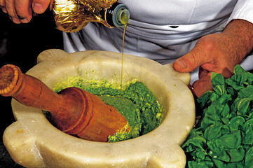 Chef pouring olive oil into marble mortar with pesto and basil