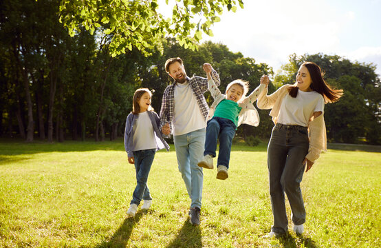 Happy family walking and playing together outdoors in summer green park, parents swinging small child, playfully kids, friendly smiling enjoying time together on sunny day weekend fun, happiness  - Powered by Adobe
