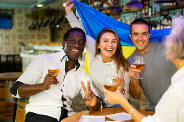Happy friends of different ages drinking beer and celebrating the victory of the Ukrainian team in the night bar