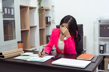 A young woman is working in a company. She puts her laptop on the table and is holding her temples. She is stressed.