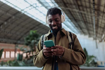 Gordijnen Tourist wearing headphones listening to music and browsing smart phone in airport © bernardbodo