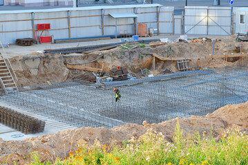 Construction site, steel rebar framework installed within an excavated trench for future concrete foundation in urban development. Foundation work, building site with steel rebar grid, excavation pit