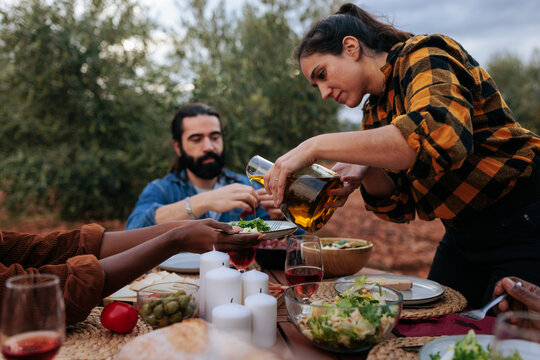 Woman pouring olive oil on salad during outdoor meal with friends in olive grove - Powered by Adobe